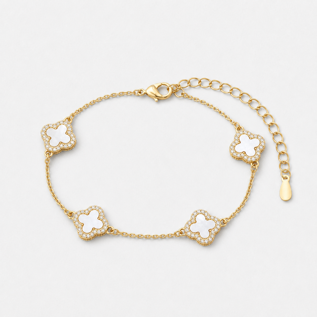 Clover bracelet with four white pearl-effect stations and clear stone borders in a gold finish on a neutral off-white background.