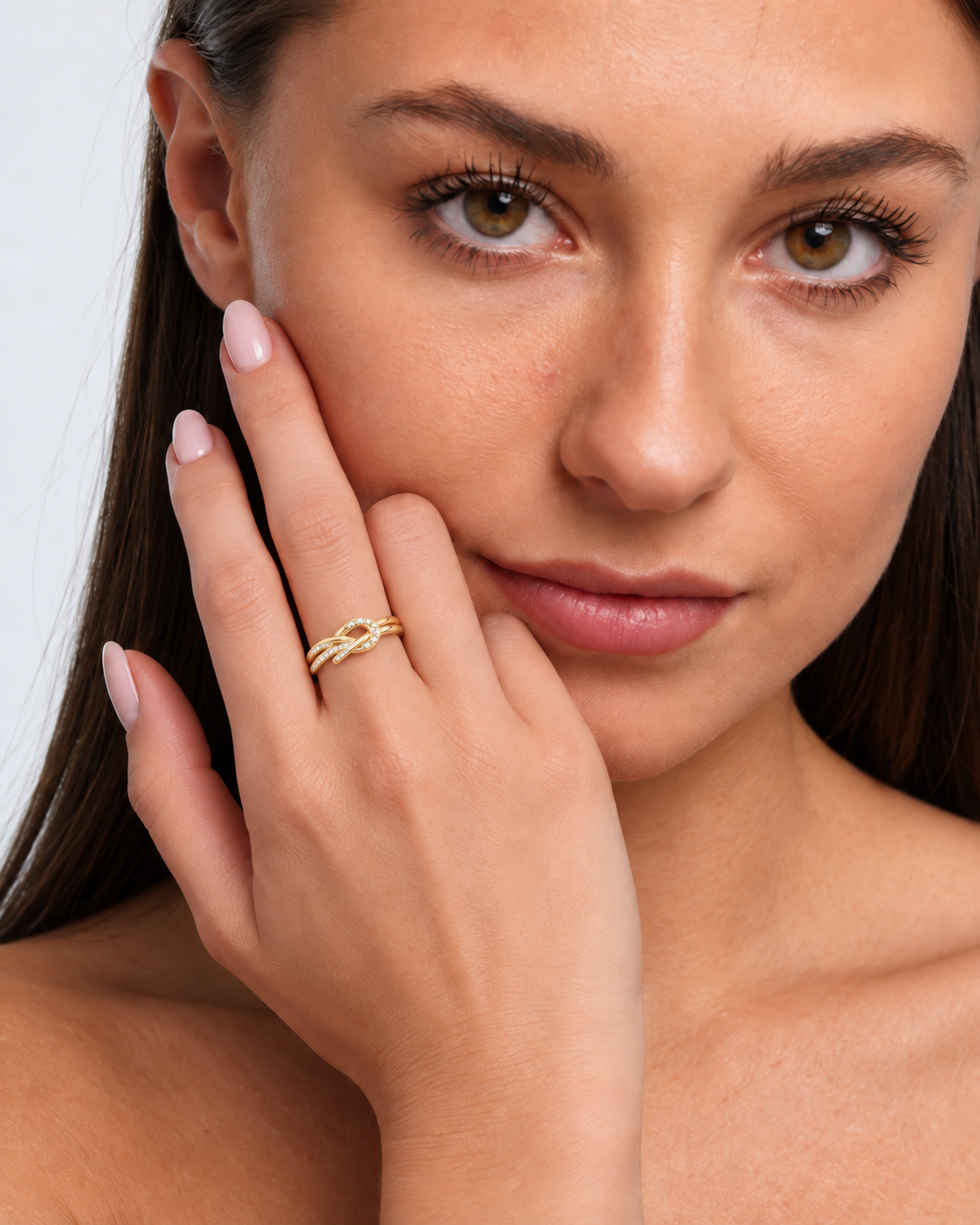 Knot adjustable ring with intertwined band and clear stone accents in a gold finish worn on the model's middle finger.