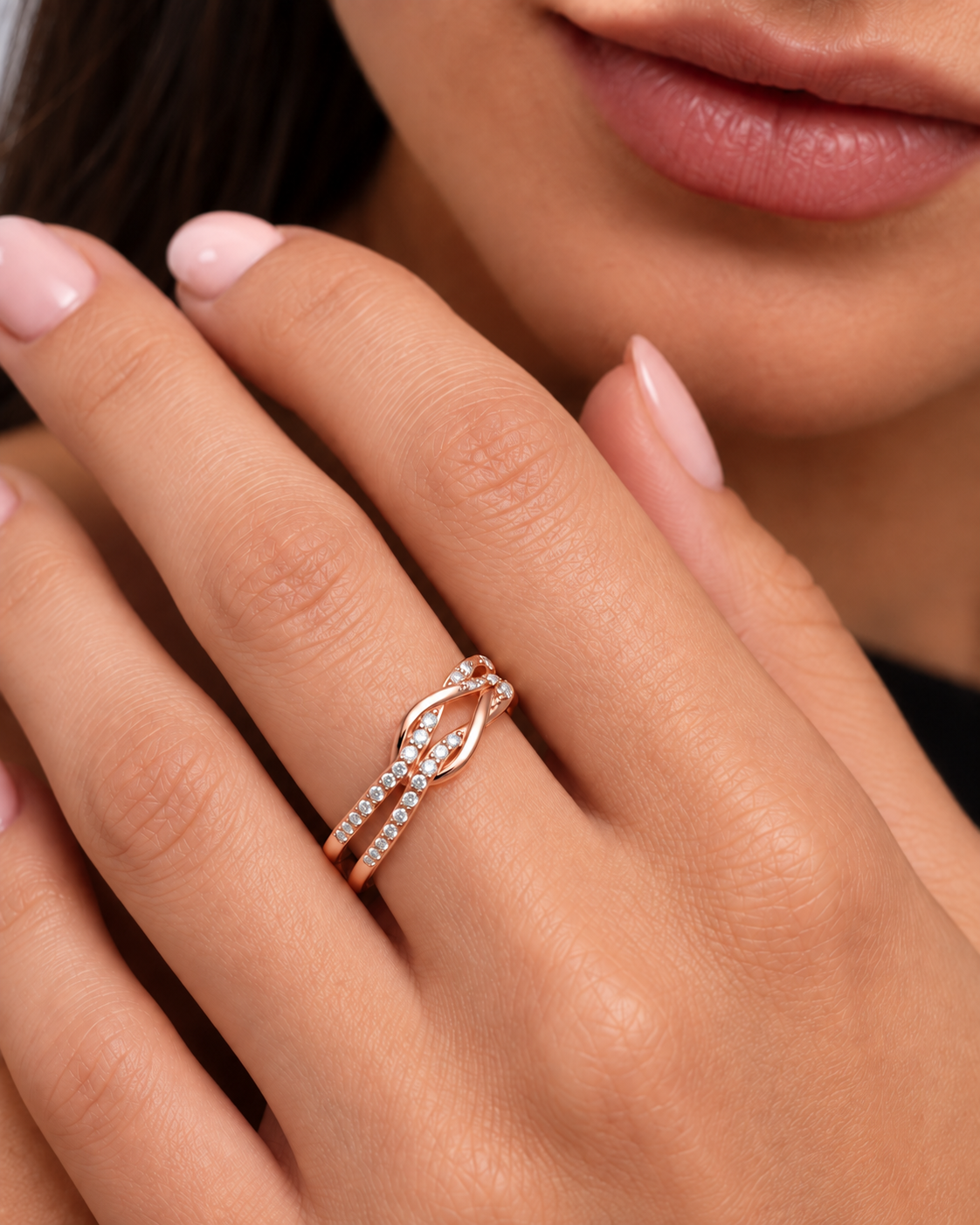 Knot adjustable ring with intertwined band and clear stone accents in a rose gold finish worn on the model's middle finger.