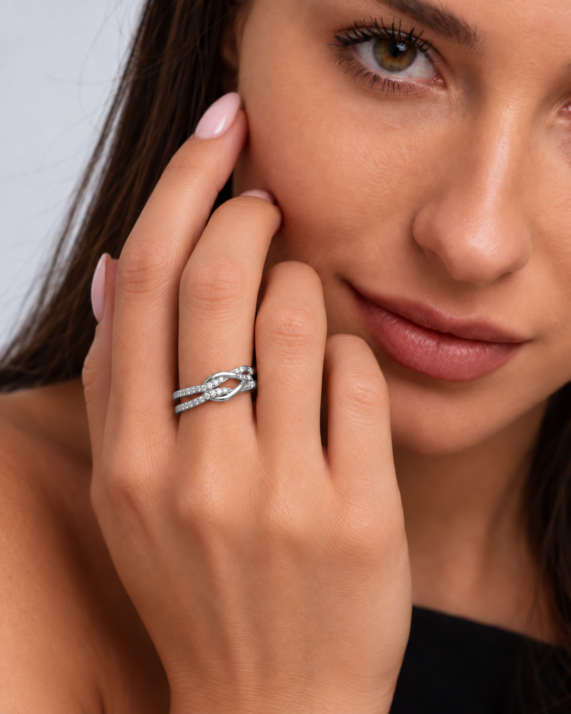 Knot adjustable ring with intertwined band and clear stone accents in a silver finish worn on the model's middle finger.
