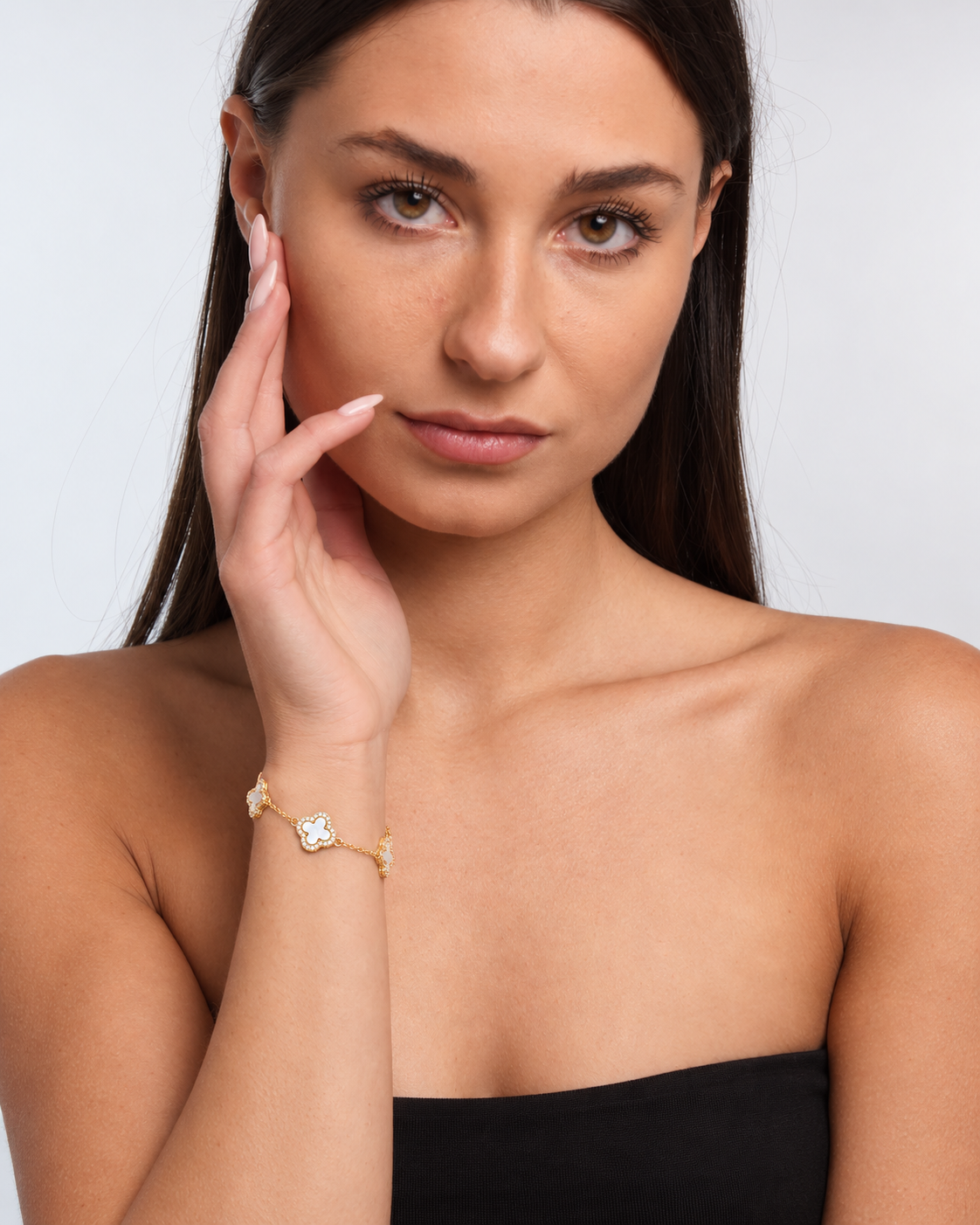 Clover bracelet with four white pearl-effect stations and clear stone borders in a gold finish worn around the model's wrist.