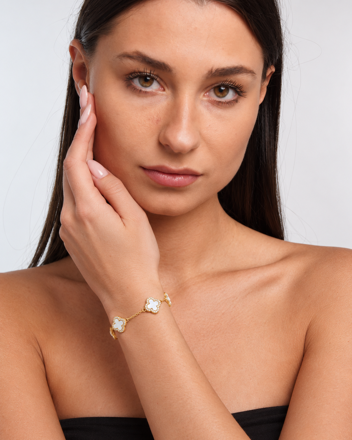 Clover bracelet with four white pearl-effect stations and clear stone borders in a gold finish worn around the model's wrist.