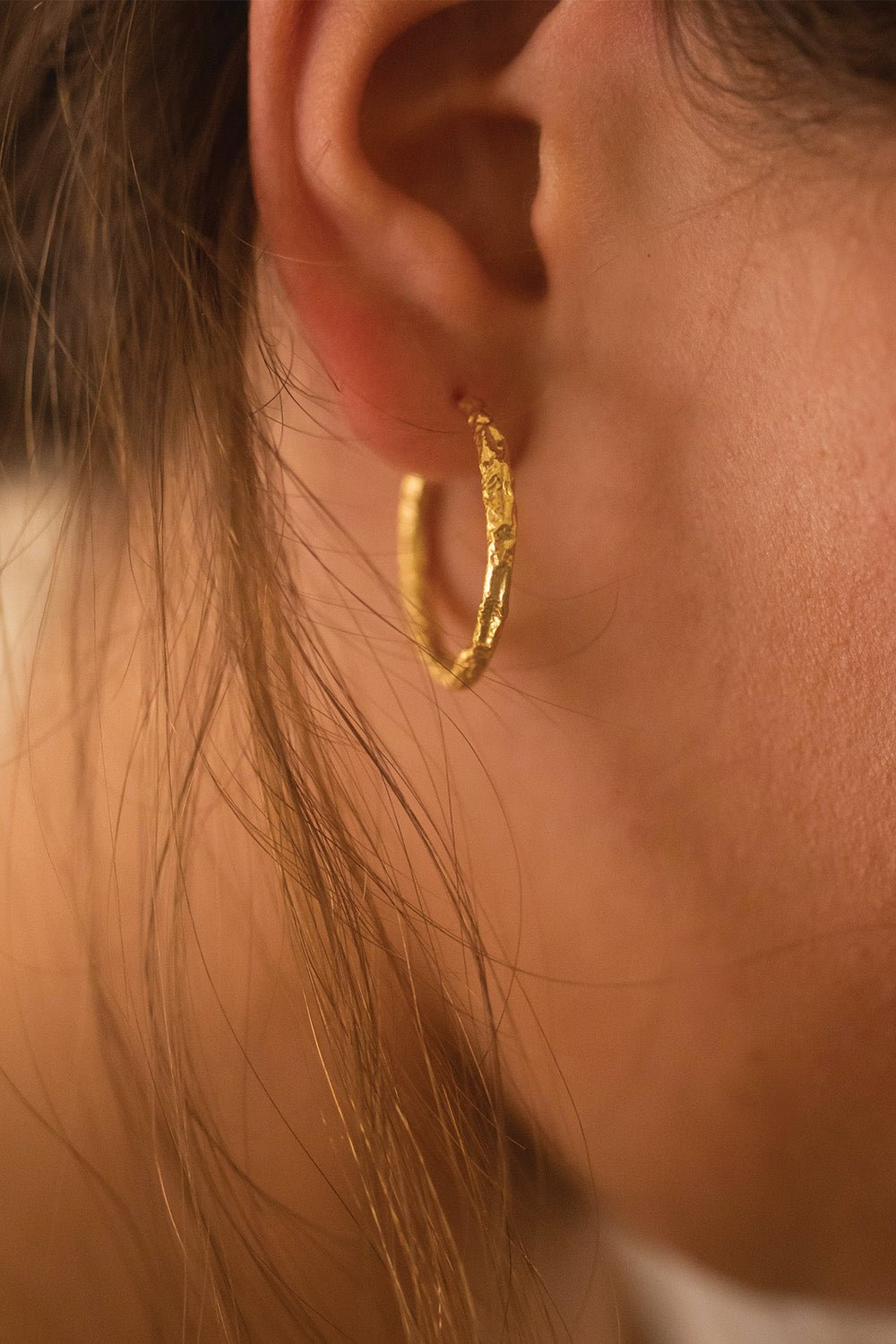 Medium gold open hoop earrings styled on a model's ear
