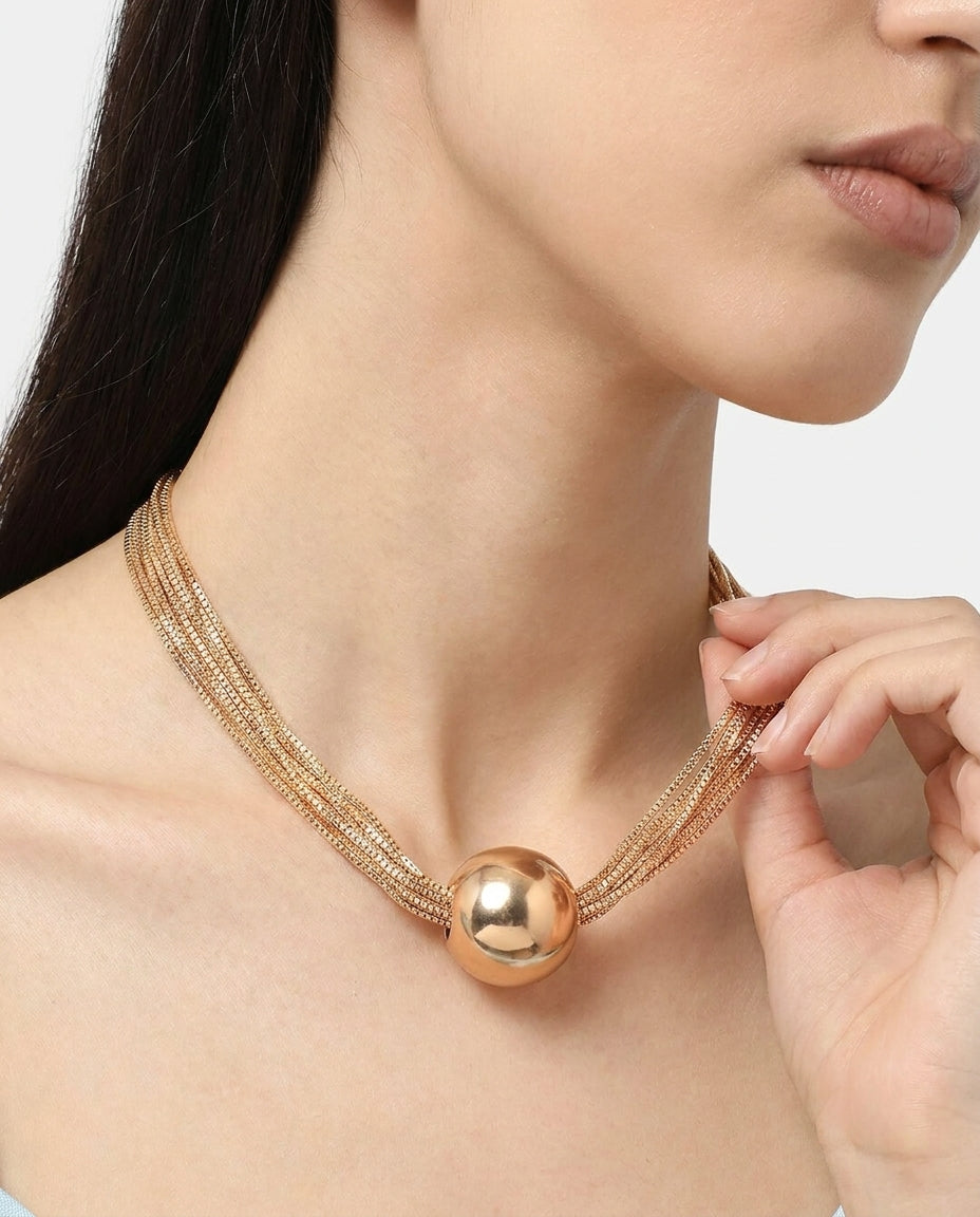 Close-up of polished gold ball pendant on layered chain