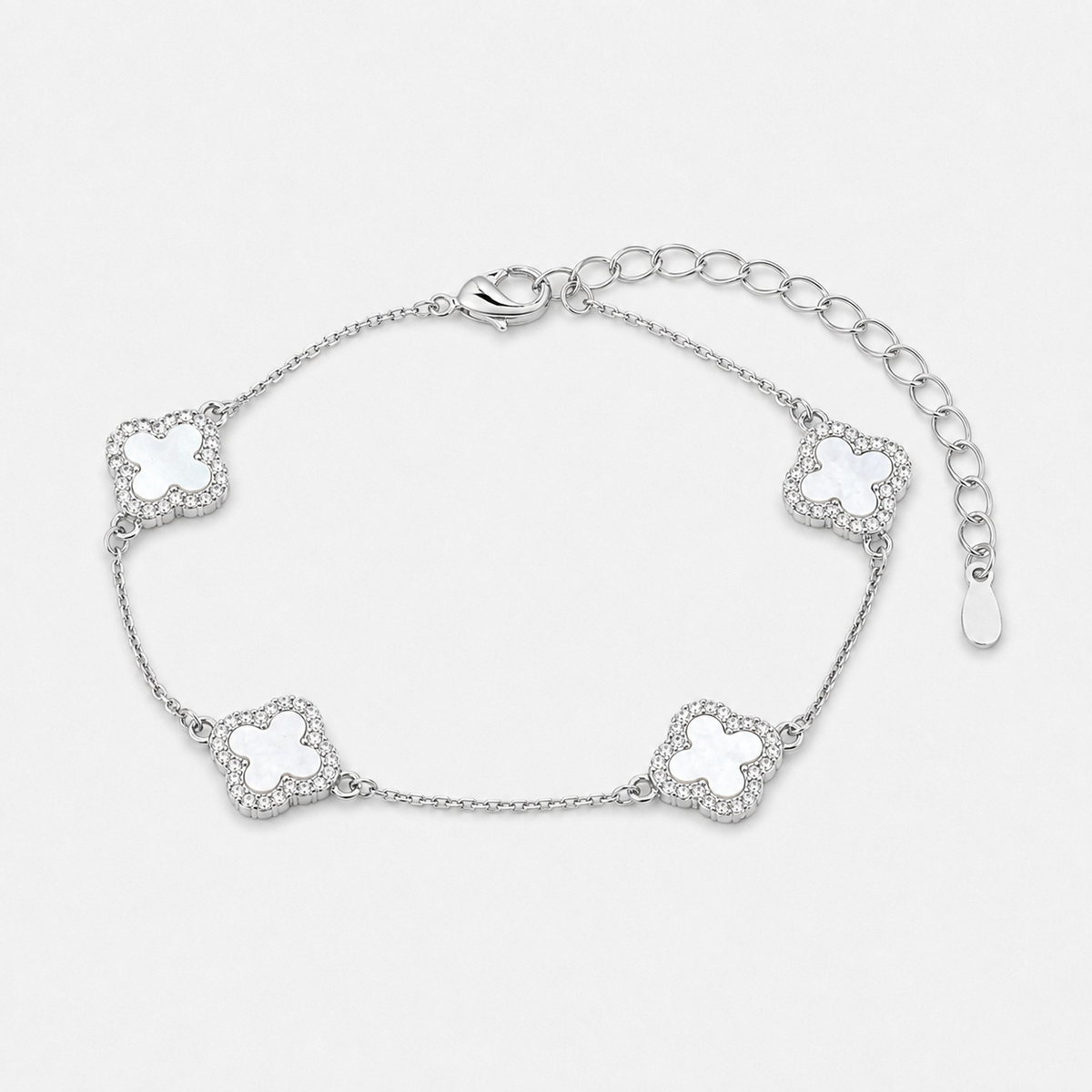 Clover bracelet with four white pearl-effect stations and clear stone borders in a silver finish on a neutral off-white background.