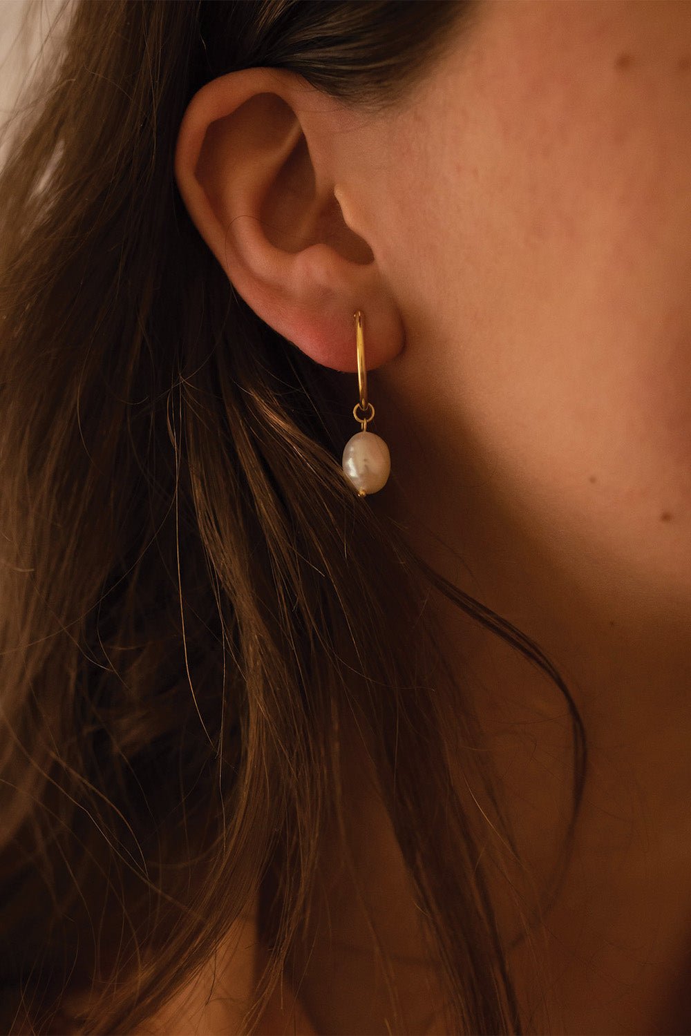 Close-up of irregular textured freshwater pearl on gold hoop earring
