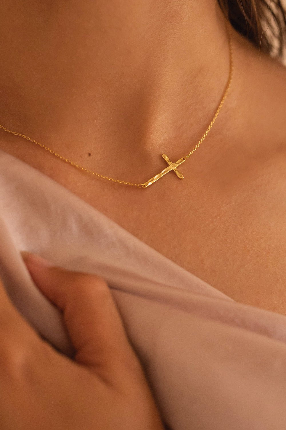 Gold cross choker styled off-centre on a model's neckline