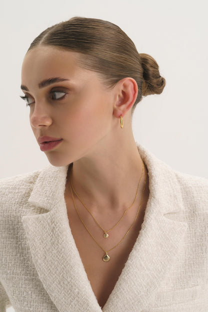 Twisted gold huggie hoop earrings styled on a model