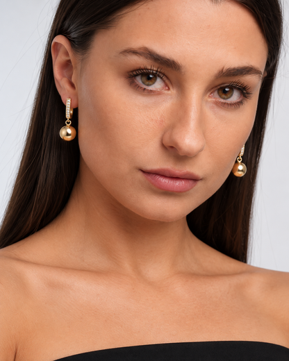 Gold-Tone Crystal Ball Drop Hoop Earrings in Gold, worn by a model in a close-up - Ravyena