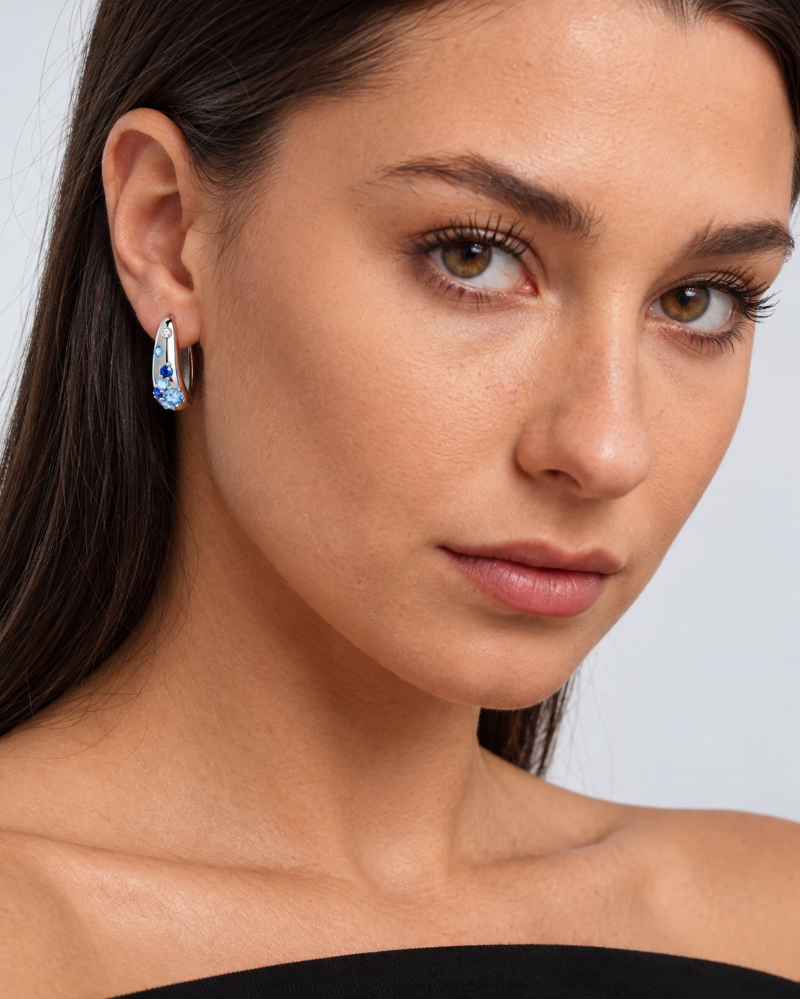 Sterling Silver Colour Crystal Hoop Earrings in Blue, worn by a model in a close-up - Ravyena