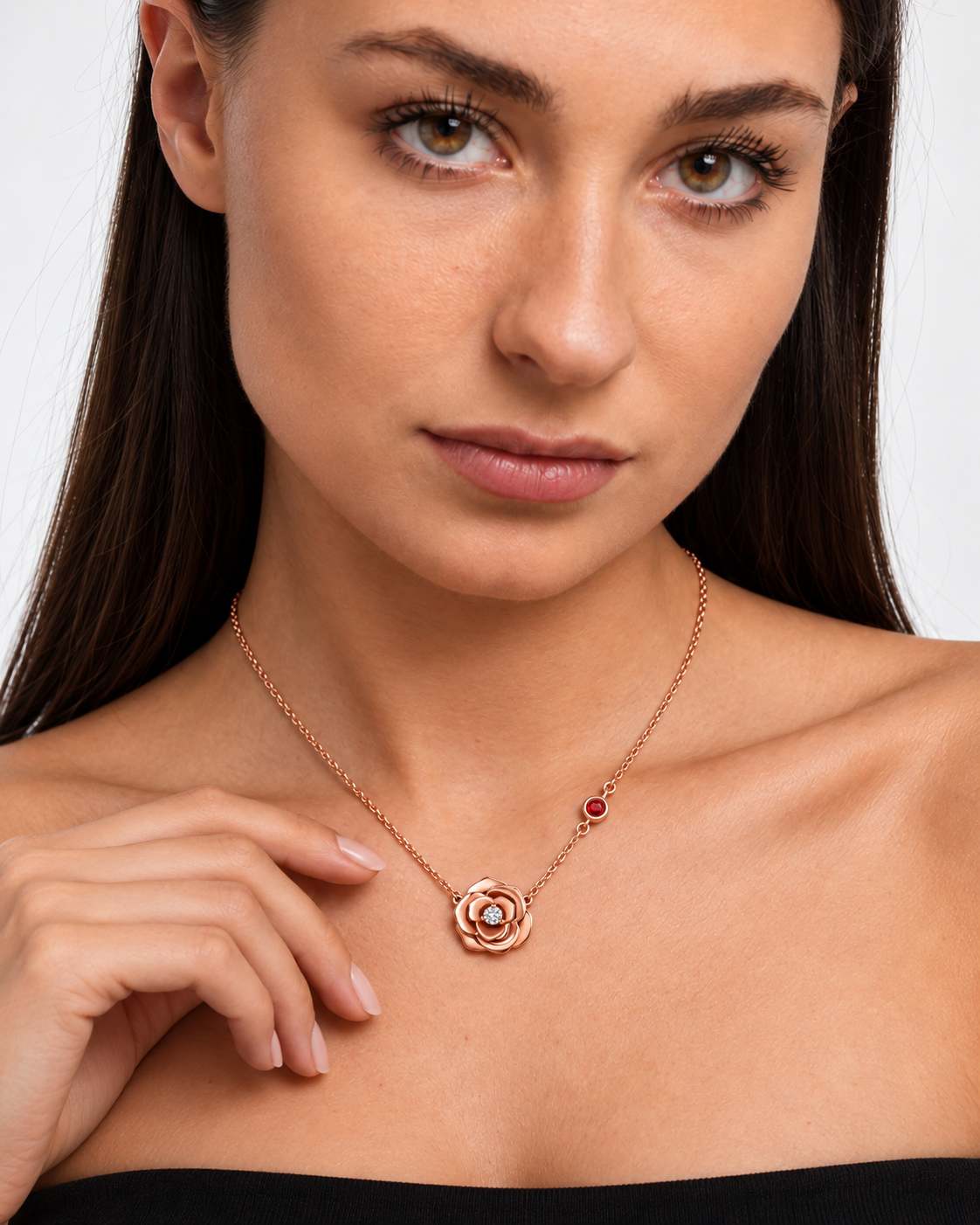 Rose pendant necklace in a rose gold colour with a clear centre stone and red chain accent worn by a brunette model, close-up detail.