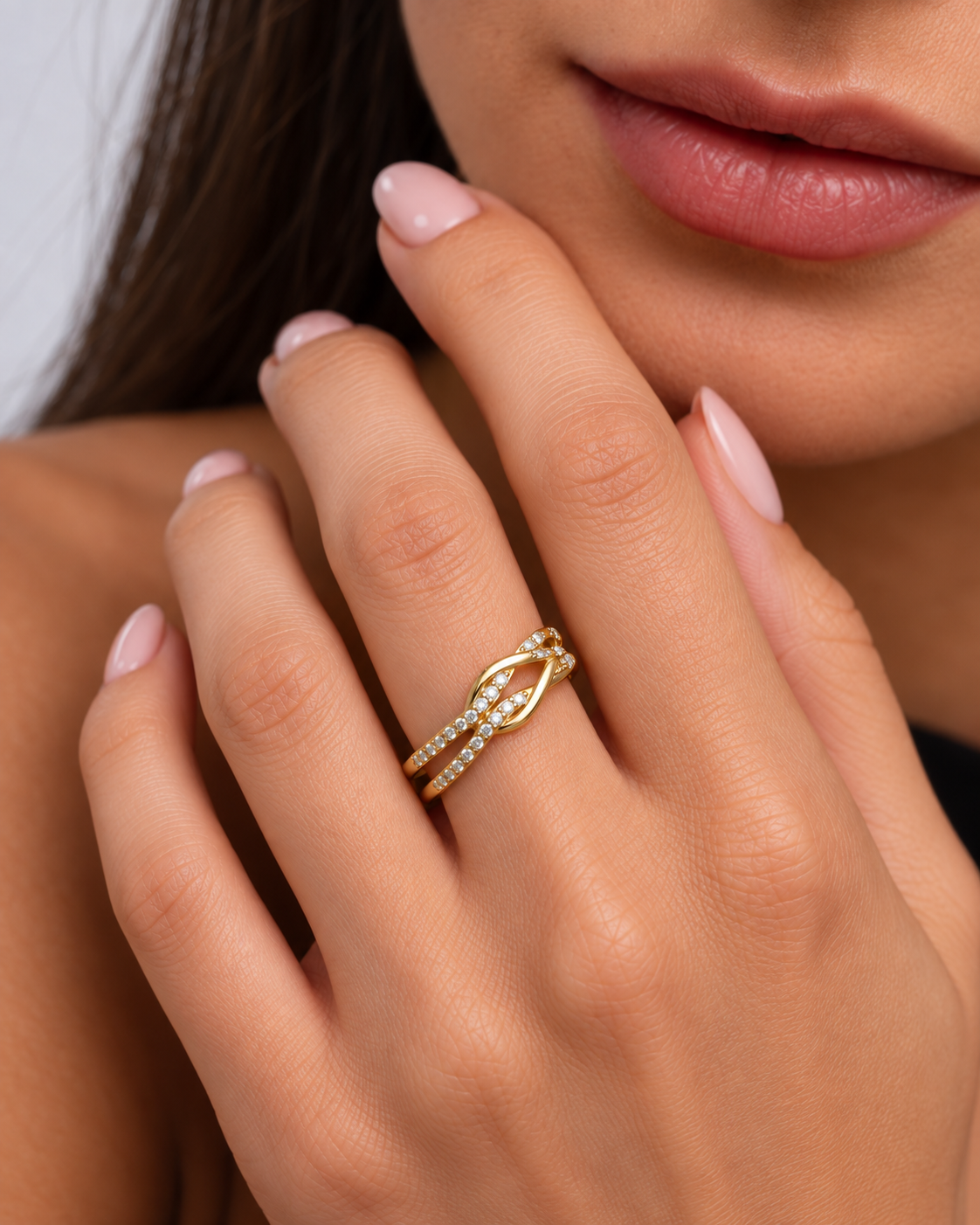 Knot adjustable ring with intertwined band and clear stone accents in a gold finish worn on the model's middle finger.