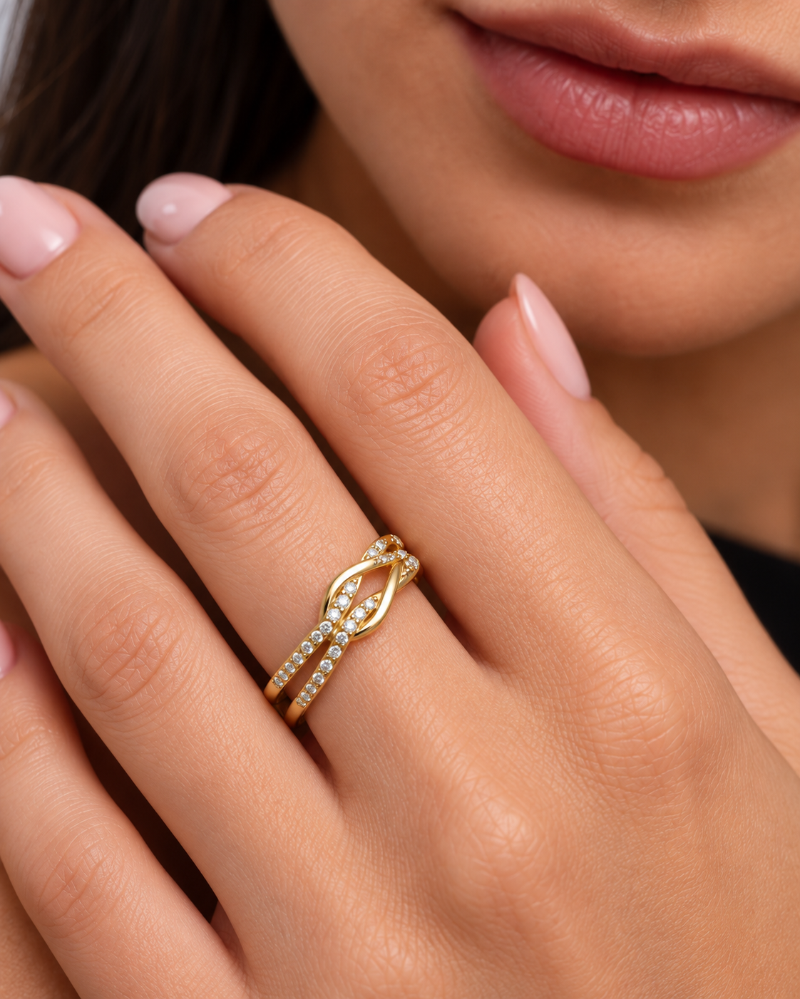 Knot adjustable ring with intertwined band and clear stone accents in a gold finish worn on the model's middle finger.