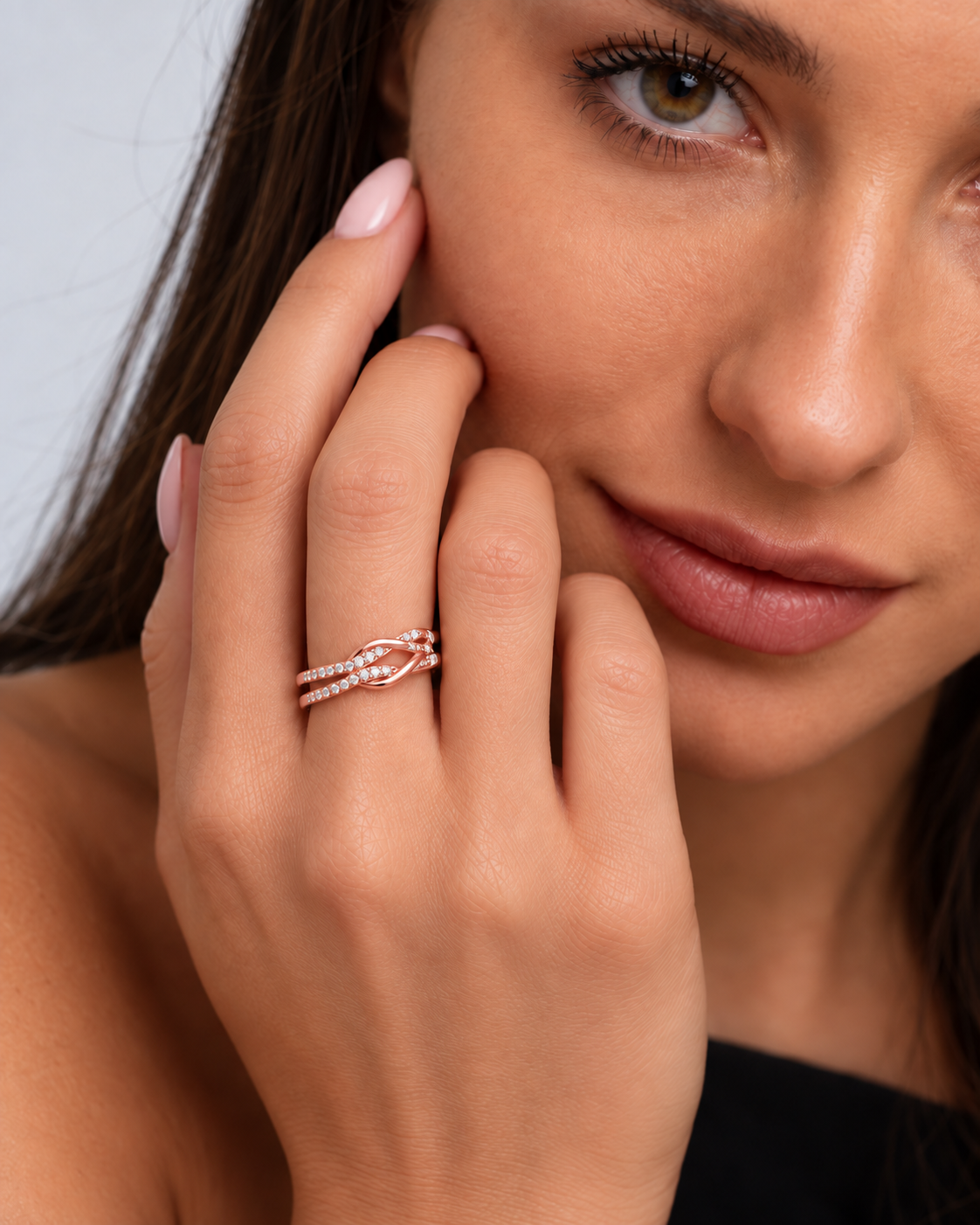 Knot adjustable ring with intertwined band and clear stone accents in a rose gold finish worn on the model's middle finger.