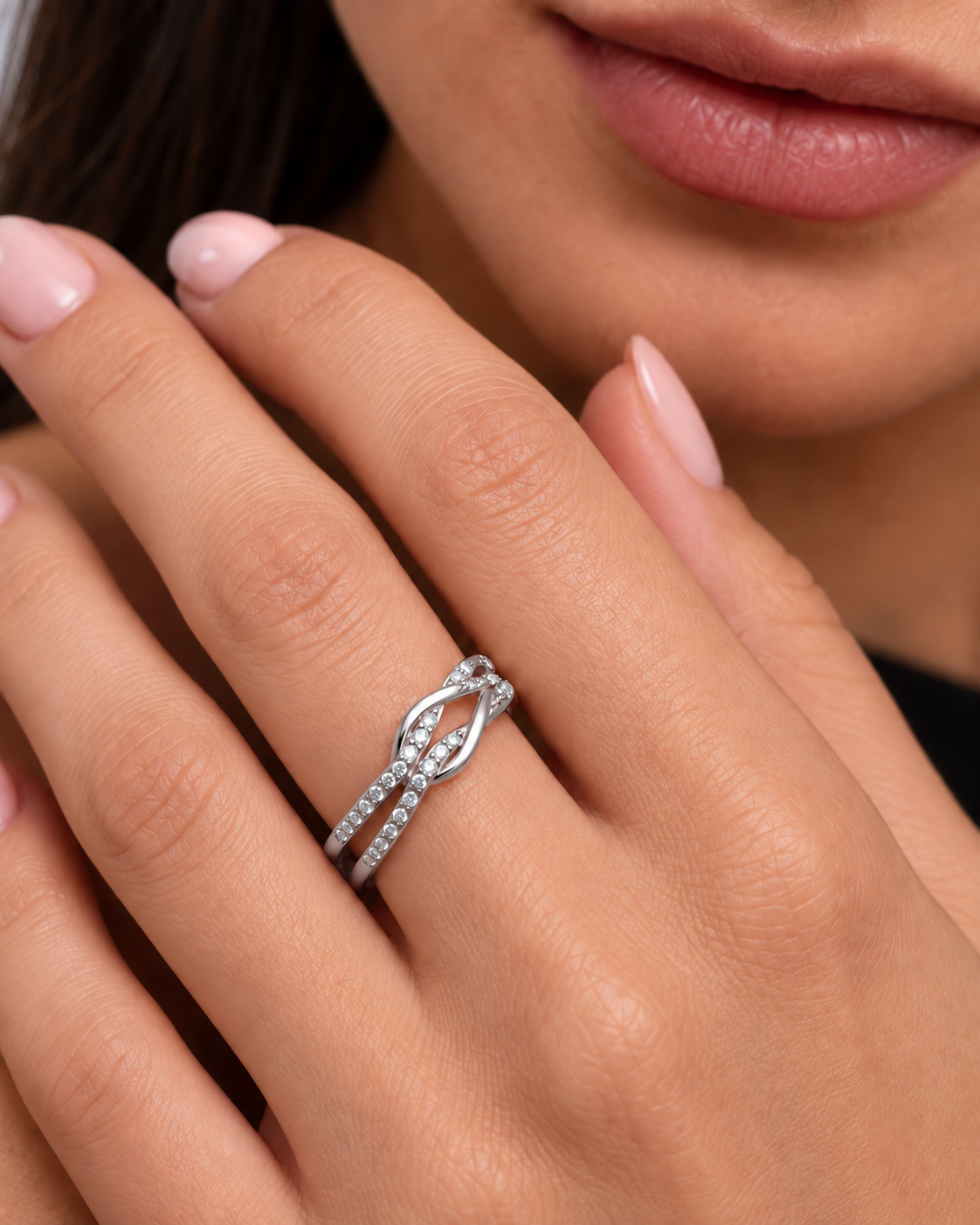 Knot adjustable ring with intertwined band and clear stone accents in a silver finish worn on the model's middle finger.