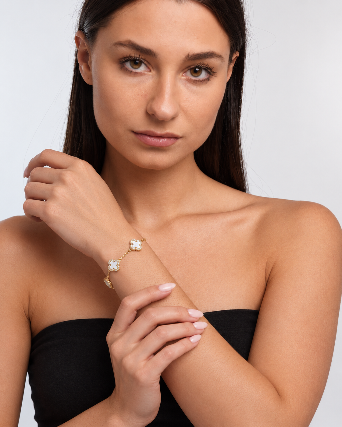 Clover bracelet with four white pearl-effect stations and clear stone borders in a gold finish worn around the model's wrist.