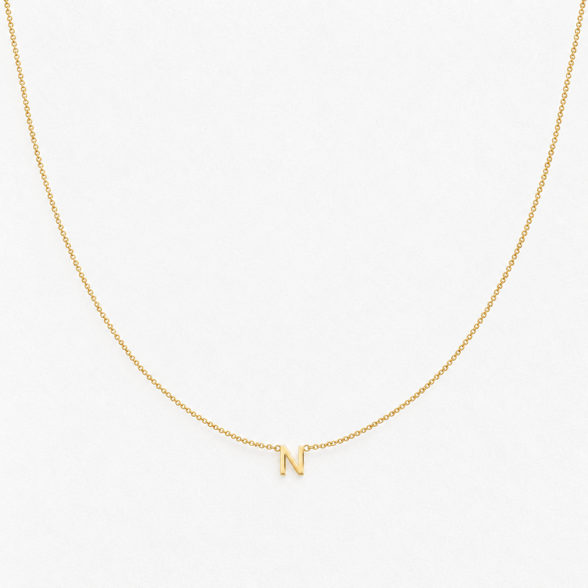 Dainty capital N initial necklace on a fine chain in a gold finish on a neutral off-white background.
