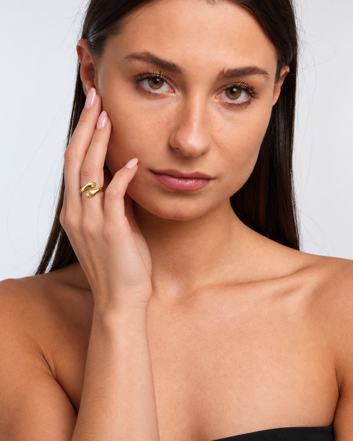 Open adjustable hug ring with two sculpted hands in a gold finish worn on the model's middle finger.