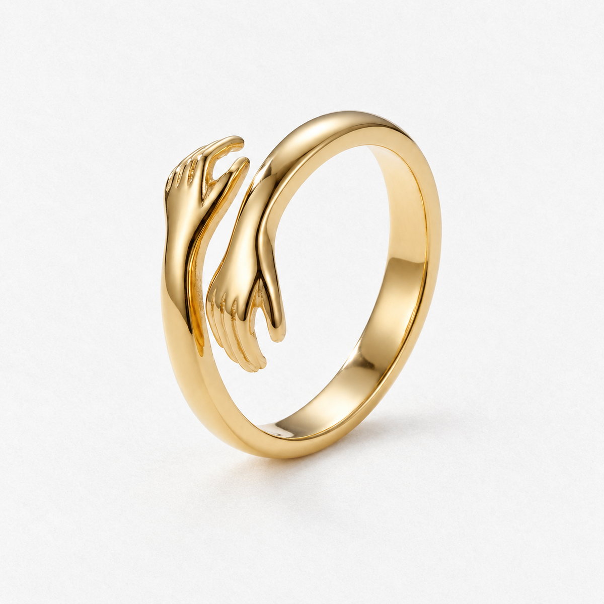 Open adjustable hug ring with two sculpted hands in a gold finish on a neutral off-white background.