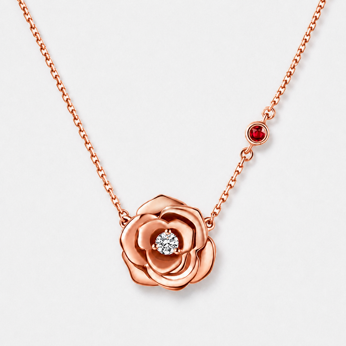 Rose flower pendant necklace with clear centre stone and red chain accent in a rose gold finish on a neutral off-white background.