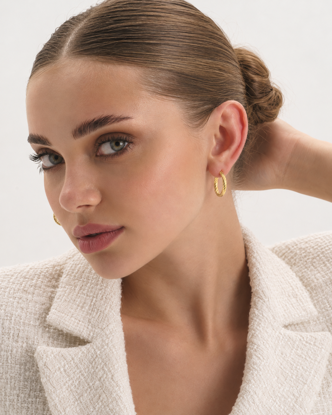 Large 14K Gold Twisted Huggie Hoop Earrings in a gold finish worn by a model, three-quarter portrait with the ear exposed
