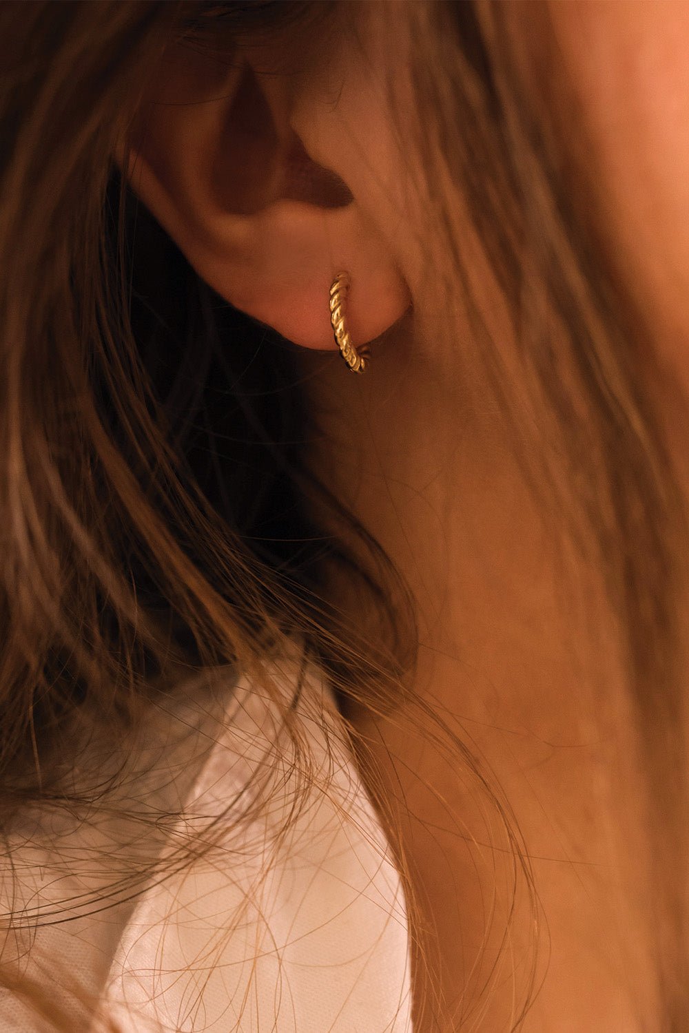 Petite gold thin hoops styled on a model's ear